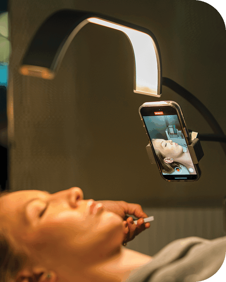 An esthetician using the GLAMCOR horizon light to provide precise and even lighting during a facial treatment.